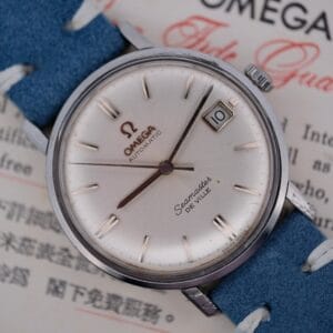 A close-up of the Omega Seamaster Deville Automatic for the Japanese Market showcases a silver dial with baton markers and a date display at 3 oclock. The watch features a blue leather strap, elegantly set against a background with text.
