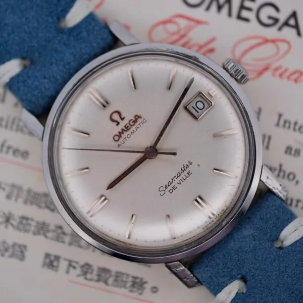 A close-up of the Omega Seamaster Deville Automatic for the Japanese Market showcases a silver dial with baton markers and a date display at 3 oclock. The watch features a blue leather strap, elegantly set against a background with text.