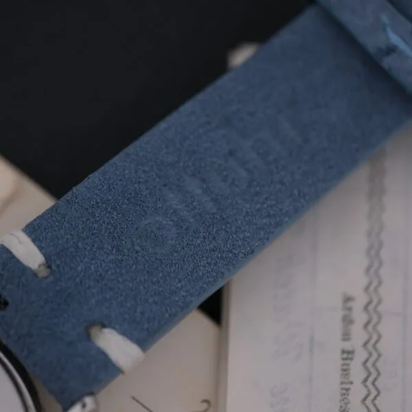 A close-up of the blue leather watch strap from the Omega Seamaster Deville Automatic for Japanese Market highlights its textured finish and stitching details, focusing on the straps stylish and durable design as it rests on paper documents.