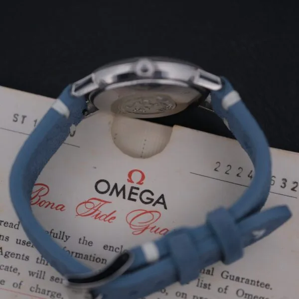 Displayed on an Omega Bona Fide Guarantee card, the vintage Omega Seamaster Deville Automatic for the Japanese market features a blue leather strap. The card shows partially visible numbers and text, while the watchs metallic backside boasts an engraved design.