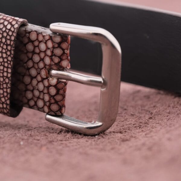 Close-up of a textured brown belt with a shiny silver buckle, echoing the Omega Deville TV Case Stainless Steels elegant design, placed on a soft brown surface.