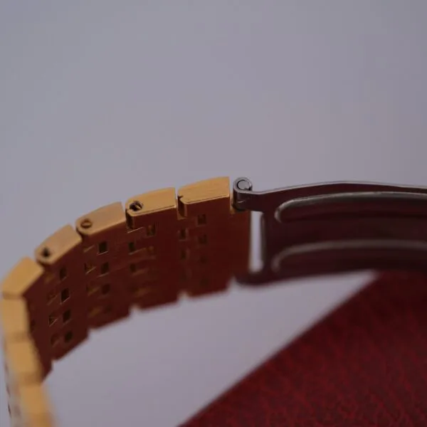 Close-up of an Omega Deville Automatic Gold Tone Date Full Set watch band on a red textured surface, highlighting the clasp mechanism.