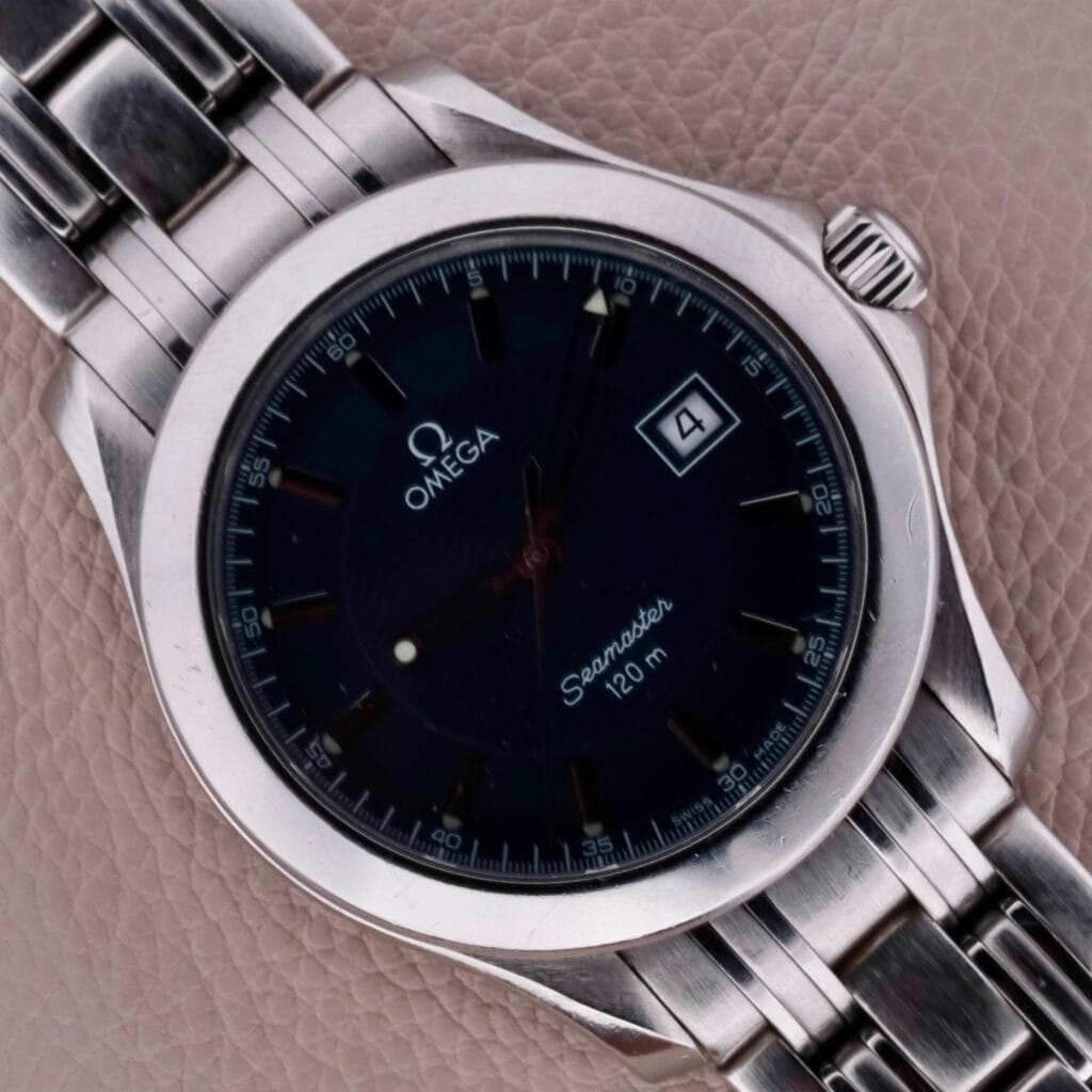 Close-up of an Omega Seamaster 120M Blue Wave with a dark face and silver bracelet, featuring a date window; it rests elegantly on a tan leather surface.