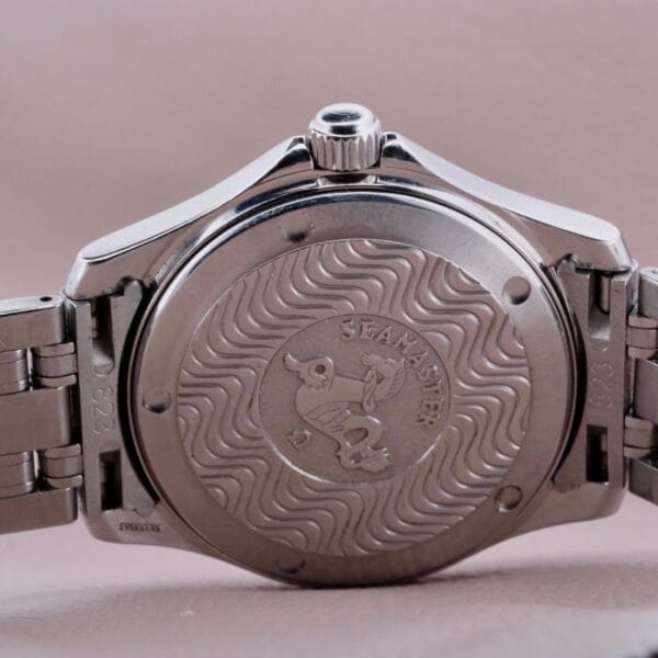 Back view of a silver Omega Seamaster 120M Blue Wave wristwatch, featuring a wave-patterned design and Seamaster engraving on the back, metal bracelet, and central crown.