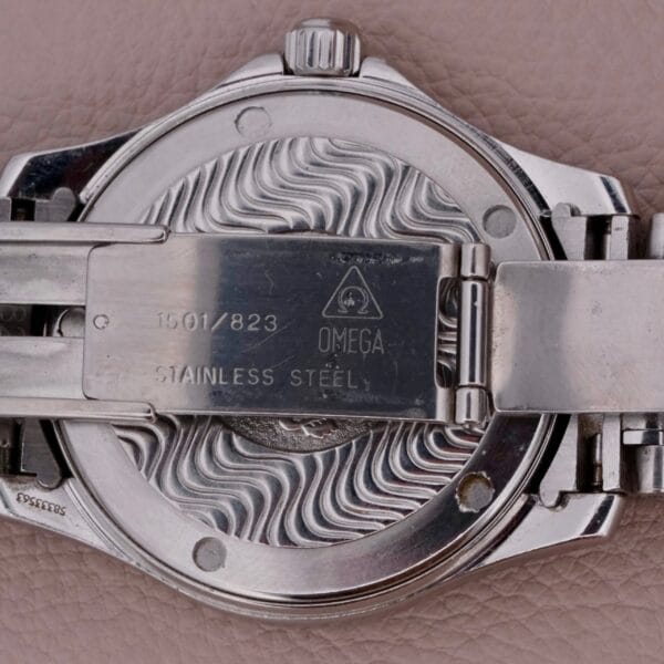 Close-up of the Omega Seamaster 120M Blue Waves back, featuring intricate wave patterns with engraved details such as Omega, Stainless Steel, and 1501/823. This stainless steel masterpiece is displayed on a textured leather surface.