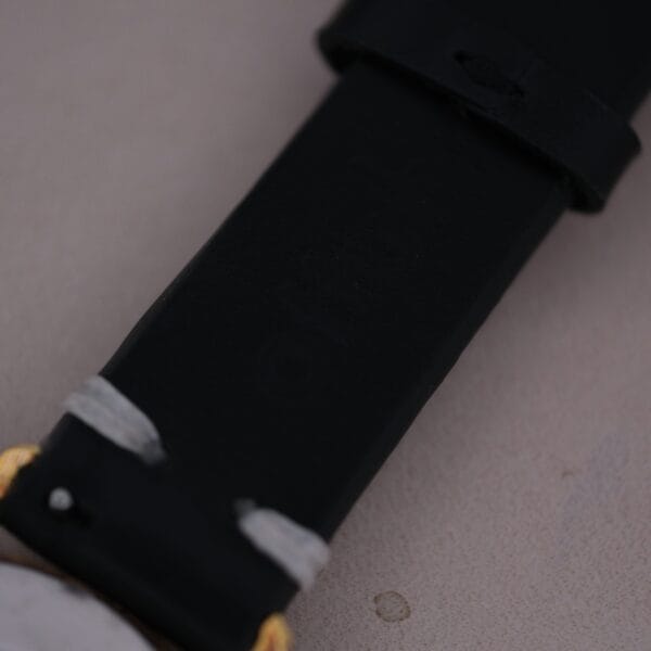 Close-up of a black strap with delicate white markings, echoing the 1960s Gruen Precision craftsmanship. The Gruen Precision 25 Jewels Auto Wind Bombay Lugs watch is elegantly set against a smooth, neutral background.