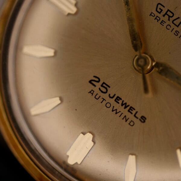Close-up of the gold-toned 1960s Gruen Precision 25 Jewels Auto Wind Bombay Lugs watch face with metallic hour markers and hands.