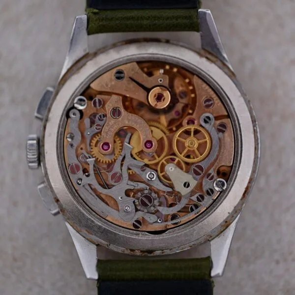 A close-up view of the Omega Turler Dial Chronograph Caliber 320 reveals its intricate gears, springs, and cogs within a metal casing. The watch features a dark green strap.