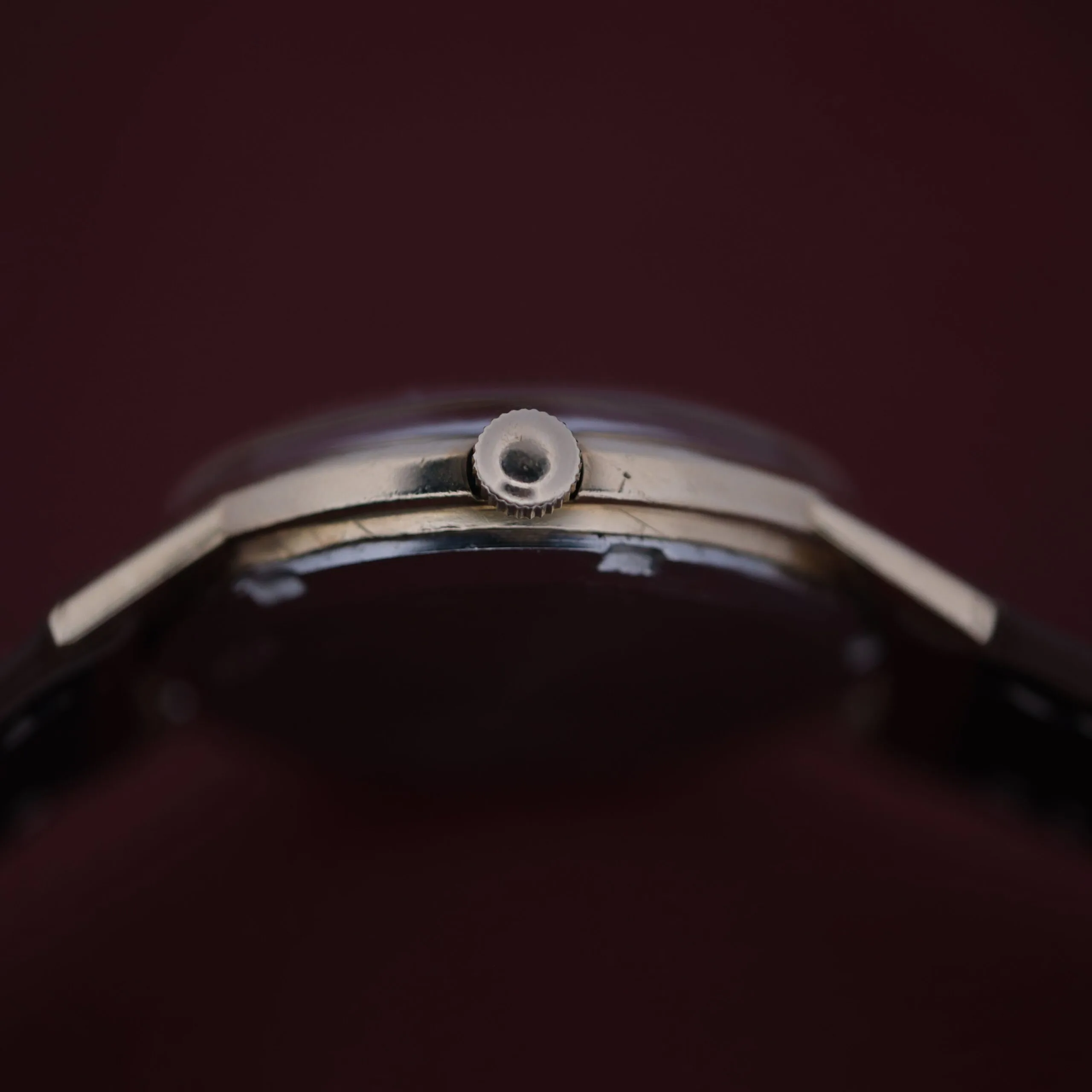 Close-up of an Omega Automatic Cal. 551 for Inland Company, highlighting its thin profile and crown with a metallic case and dark strap, elegantly set against a rich dark brown background.