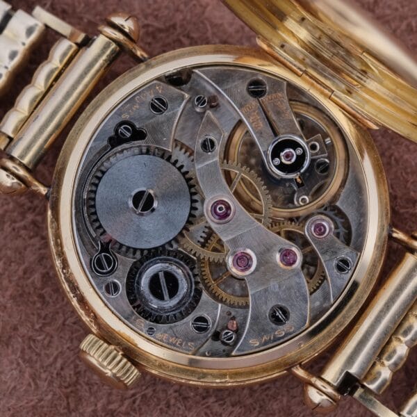 Close-up of an open Cartier Officer Watch 18k Gold Roman Numerals Edmond Jager revealing intricate metallic gears, screws, and a partially visible winding mechanism against a textured brown background.