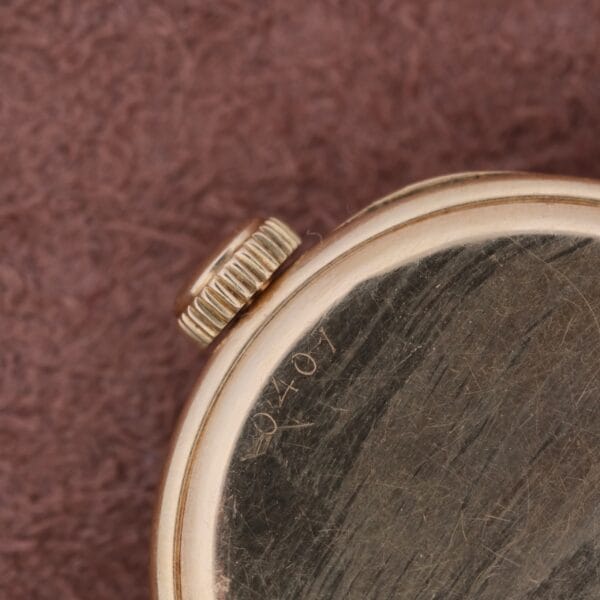 Close-up of a Cartier Officer Watch 18k Gold Roman Numerals Edmond Jager, highlighting its winding crown and case. The gold appears slightly worn with faint engravings, set against a soft, textured brown fabric that enhances its vintage charm.