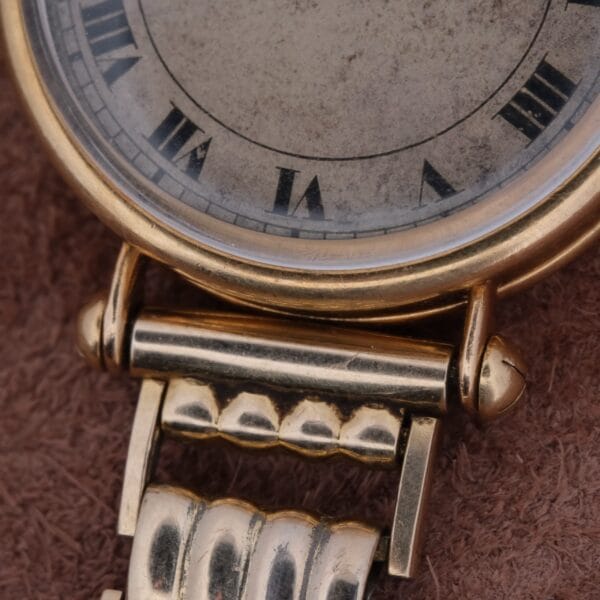 A close-up of a Cartier Officer Watch in 18k gold, featuring Roman numerals by Edmond Jager. The watch rests on a textured brown surface, showcasing its vintage design.