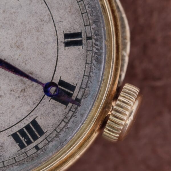 Close-up of a vintage Cartier Officer Watch 18k Gold Roman Numerals Edmond Jager, featuring dark blue hands and a weathered face showing approximately 1:55. The gold-toned case rests elegantly on a textured brown surface, exuding timeless sophistication.