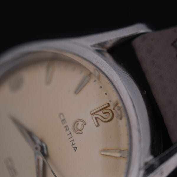 Close-up of the Certina DS 1st Gen Cal. 25-36 Stainless Steel wristwatch with a beige dial, focusing on the number 12 and part of the metal case, highlighting worn edges and a leather strap.