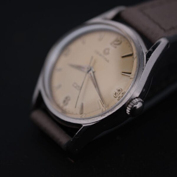 Close-up of a vintage Certina DS 1st Gen Cal. 25-36 wristwatch, featuring a cream dial, silver casing, simple silver markers and hands. It comes with a brown leather strap and displays the Certina logo with subtle text.