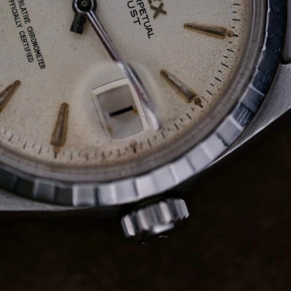 Close-up of a vintage Rolex Oyster Perpetual Datejust 6605 Cal. 1066 wristwatch. The off-white face features an angular date aperture and silver hour markers, while the slightly worn metallic bezel enhances its elegant, aged charm.
