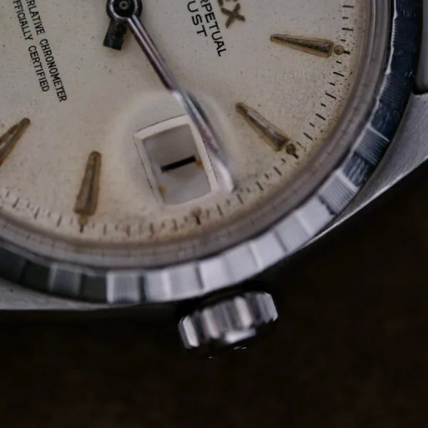 Close-up of a vintage Rolex Oyster Perpetual Datejust 6605 Cal. 1066 wristwatch. The off-white face features an angular date aperture and silver hour markers, while the slightly worn metallic bezel enhances its elegant, aged charm.