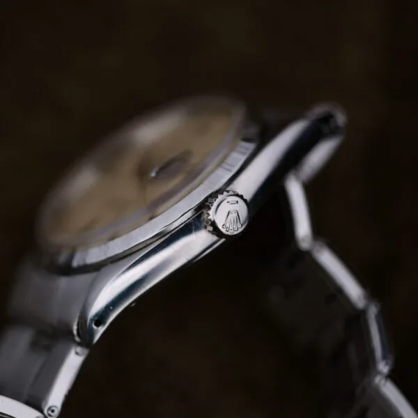 Close-up of a silver Rolex Oyster Perpetual Datejust 6605 Cal. 1066 wristwatch, highlighting the crown with part of the watch face visible. The timepiece has a metallic band set against a dark, blurred background.