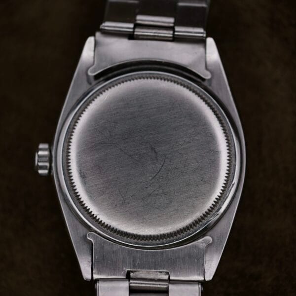 Close-up of the back of a Rolex Oyster Perpetual Datejust 6605 Cal. 1066 with brushed stainless steel. The watch features a round face, and its metal band shows a side view of the crown with subtle surface scratches and marks.