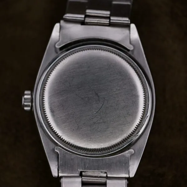 Close-up of the back of a Rolex Oyster Perpetual Datejust 6605 Cal. 1066 with brushed stainless steel. The watch features a round face, and its metal band shows a side view of the crown with subtle surface scratches and marks.