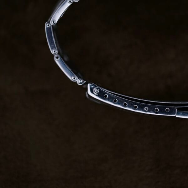 A close-up image of the Rolex Oyster Perpetual Datejust 6605 Cal. 1066 watchs metallic strap against a dark background shows small screws and links polished to a shiny finish.