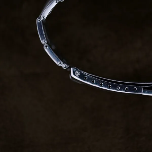 A close-up image of the Rolex Oyster Perpetual Datejust 6605 Cal. 1066 watchs metallic strap against a dark background shows small screws and links polished to a shiny finish.