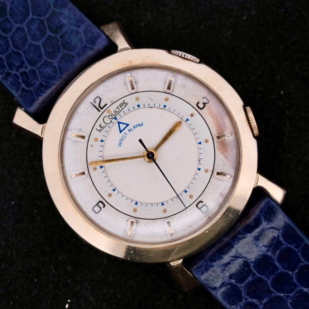 Lecoultre Wrist Alarm watch featuring a gold casing, blue leather strap, and dial set to 7:20.