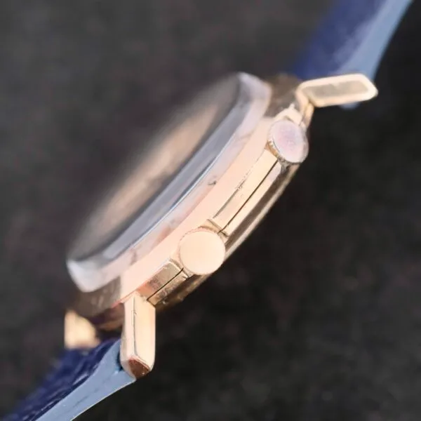 Close-up of a Lecoultre Wrist Alarm featuring its crown and buttons on a blue strap set against a dark background.