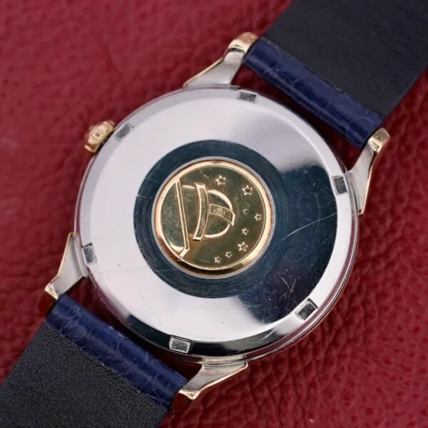 The Omega Constellation Pie-Pan Automatic 561 features a circular gold medallion on the back with a dome and star design set against a textured red background, complemented by an elegant black leather strap.