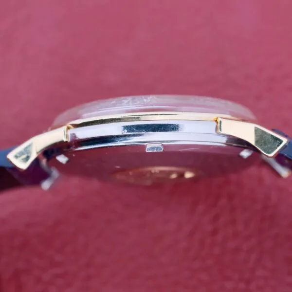 Close-up side profile of the Omega Constellation Pie-Pan Automatic 561, featuring a transparent back cover and gold-tone accents. It rests on a textured red surface, emphasizing the watchs craftsmanship details.