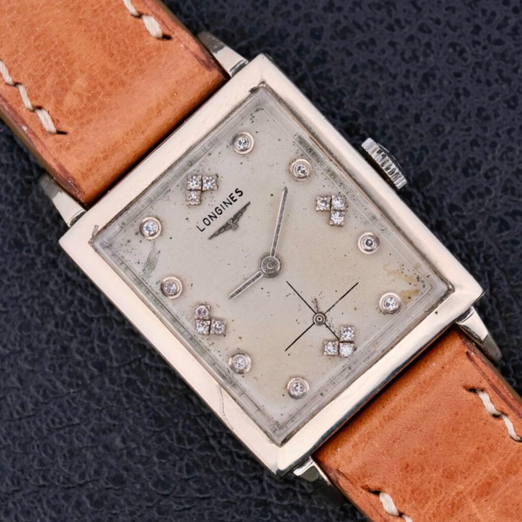 A Longines Tank 14k White Gold Diamond Dial Cal. 370 watch with a tan leather strap rests on a dark textured surface.