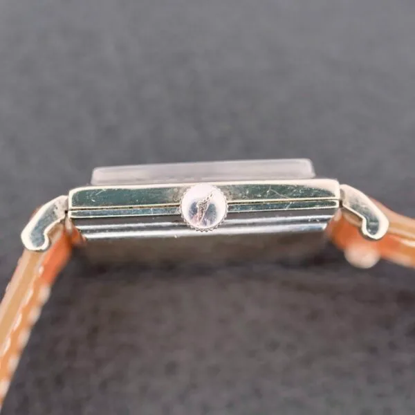 Close-up of the Longines Tank 14k White Gold Diamond Dial Cal. 370 wristwatch from the side. The rectangular case with a worn silver-tone crown and leather straps on both sides against a textured dark surface embodies timeless elegance.