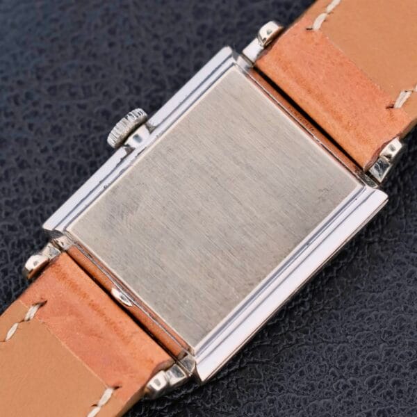 A close-up of the Longines Tank 14k White Gold Diamond Dial Cal. 370 wristwatch shows its light brown leather strap and stainless steel case with a brushed finish, elegantly placed on a dark, textured surface.