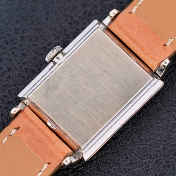 A close-up of the Longines Tank 14k White Gold Diamond Dial Cal. 370 wristwatch shows its light brown leather strap and stainless steel case with a brushed finish, elegantly placed on a dark, textured surface.
