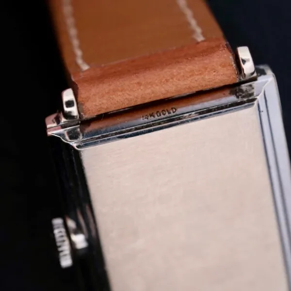 Close-up of the back of a Longines Tank, showcasing its silver rectangular case with 14K GOLD engraving. The watch features a brown leather strap and emphasizes the seamless connection between strap and case, reminiscent of its iconic design.