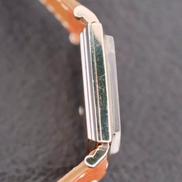 Side view of a Longines Tank 14k White Gold Diamond Dial Cal. 370 watch with a clear crystal and brown leather strap, placed on a black surface, highlighting its sleek and minimalist design.