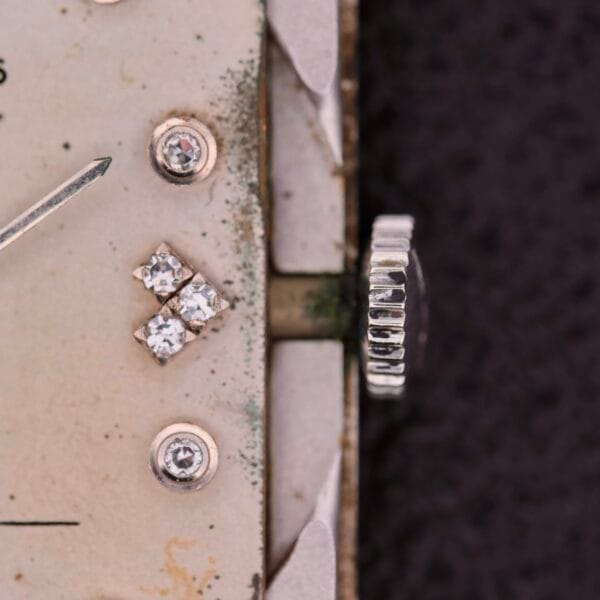 Close-up of a vintage Longines Tank 14k White Gold Diamond Dial Cal. 370 watch face with a tarnished, off-white dial. It features small diamond markers and a decorative crown, exemplifying timeless elegance with its gracefully aged surface.