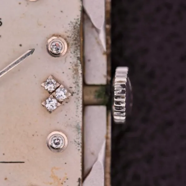 Close-up of a vintage Longines Tank 14k White Gold Diamond Dial Cal. 370 watch face with a tarnished, off-white dial. It features small diamond markers and a decorative crown, exemplifying timeless elegance with its gracefully aged surface.