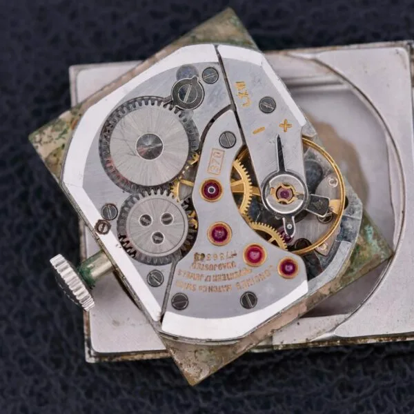 A close-up reveals the intricate mechanism of the Longines Tank 14k White Gold Diamond Dial Cal. 370, showcasing visible gears, screws, and jewels against a black backdrop. The metallic components are compactly arranged in its rectangular Tank formation, highlighting the engineering marvel.