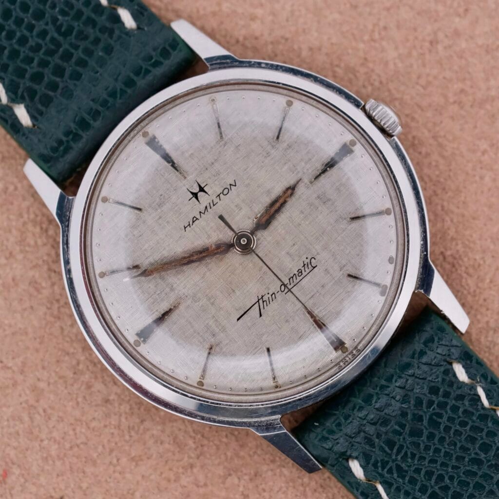 A vintage Hamilton Thin-O-Matic Linen Dial T-502 Micro-Rotor wristwatch with a worn dial and a textured green leather strap.