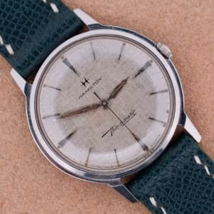 A vintage Hamilton Thin-O-Matic Linen Dial T-502 Micro-Rotor wristwatch with a worn dial and a textured green leather strap.