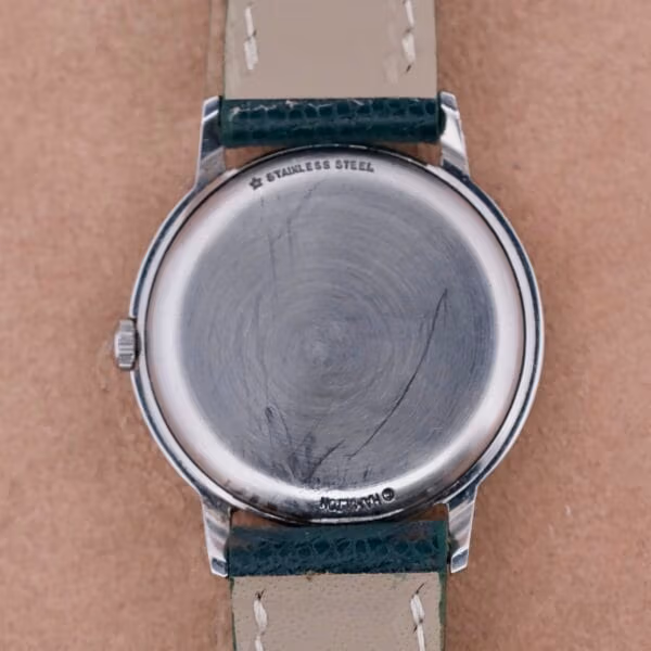 The image showcases a Hamilton Thin-O-Matic Linen Dial T-502 Micro-Rotor. The stainless steel case back displays visible scratches, while the leather strap with contrasting stitching enhances its classic look. Its round design features a crown on the left side, embodying timeless elegance.