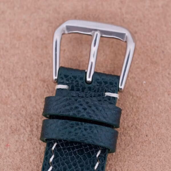 Close-up of a green leather watch strap with a silver buckle, inspired by the classic Hamilton Thin-O-Matic Linen Dial T-502 Micro-Rotor. Featuring two loops and white stitching, it contrasts beautifully against a neutral beige background.