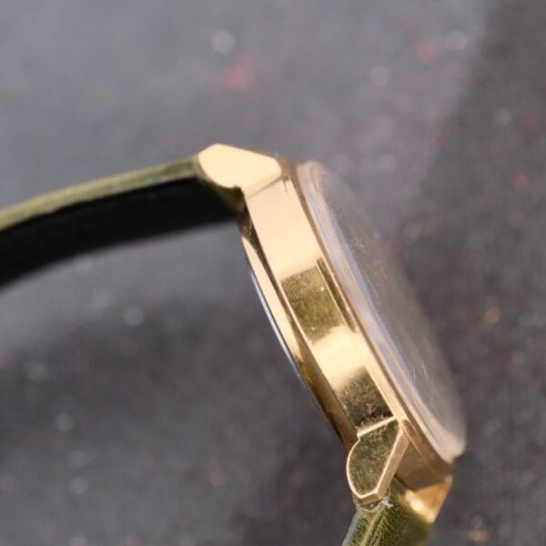 Side view of a Benrus Citation Automatic Chronometer Date wristwatch, highlighting its green leather strap and glossy glass face, elegantly set against a dark, textured background.