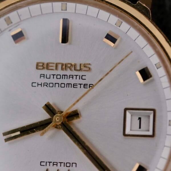 Close-up of a Benrus Citation Automatic Chronometer Date watch face with gold hour markers and hands, a white background, and a date window at three oclock displaying 1. The words AUTOMATIC CHRONOMETER and CITATION are elegantly inscribed.