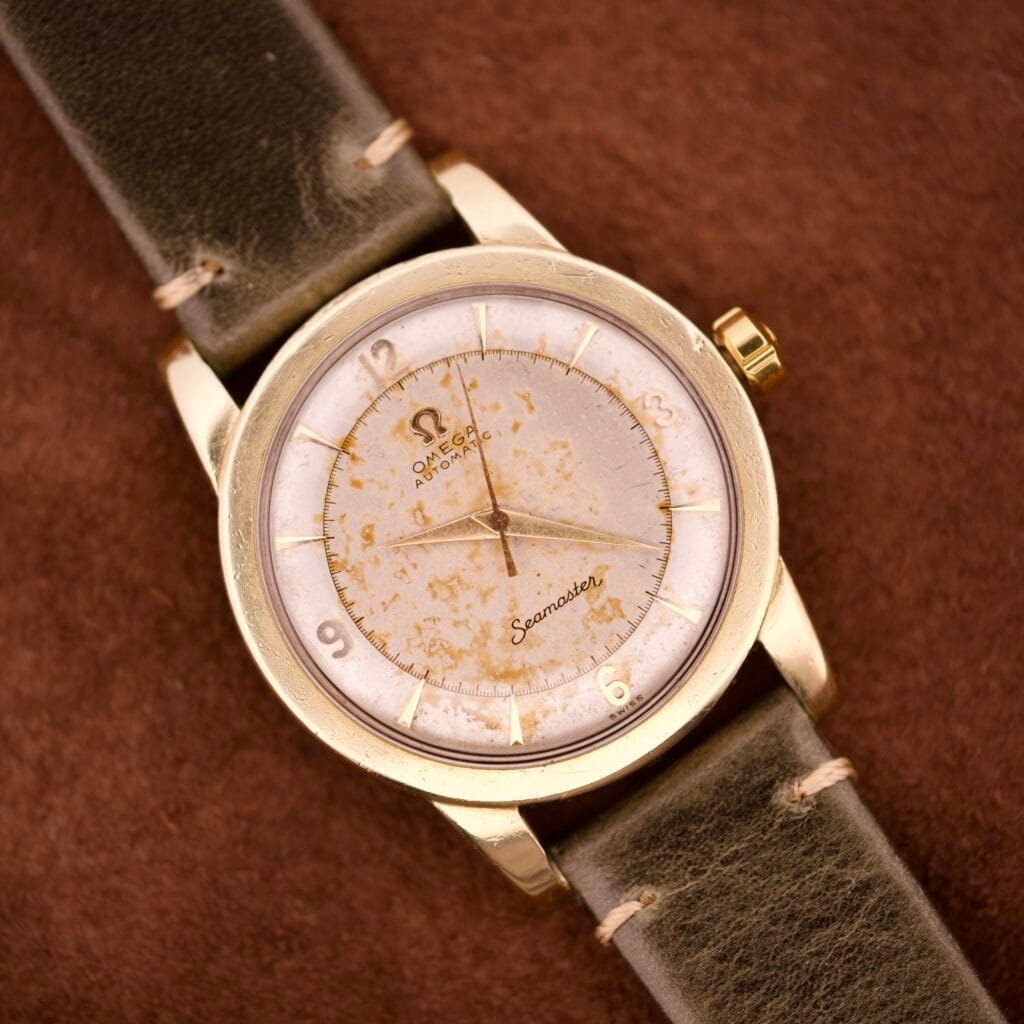 An Omega Seamaster Gold Automatic 354 with a worn dial and leather strap rests elegantly on a brown surface.