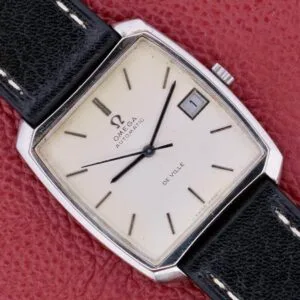 An Omega Deville Automatic with a tonneau case and black leather strap rests elegantly on a red textured surface.