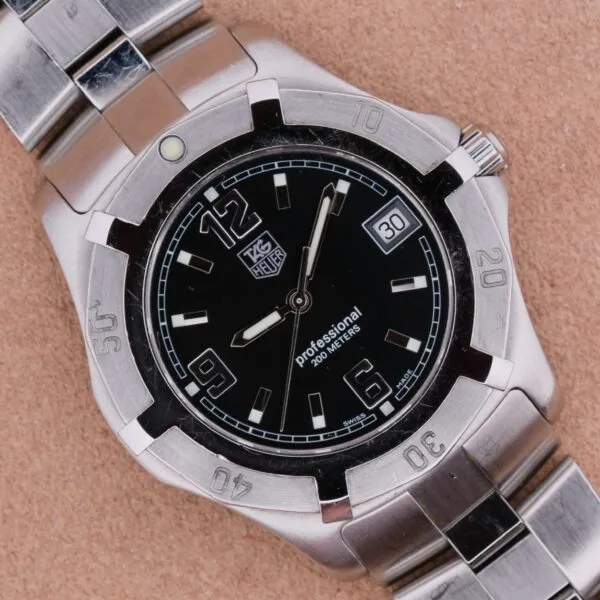 The Tag Heuer Professional Dive watch has a silver metal wristband, black dial with white numerals at 12, 9, and 6 oclock, and a date display at 3 oclock. Its water-resistant up to 200 meters and features a scratch-resistant bezel.