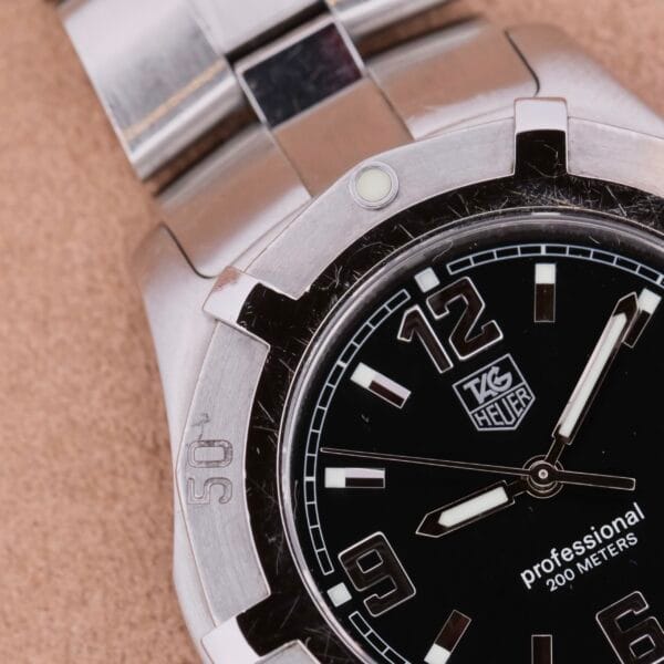 A close-up of the Tag Heuer Professional Dive watch reveals a silver stainless steel band and black dial featuring white hour markers, numerals, and the brand logo. With professional 200 meters marked on it, this expertly crafted timepiece embodies elegance and functionality.