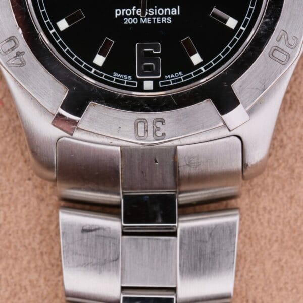 Close-up of a Tag Heuer Professional Dive stainless steel watch with a black dial, featuring professional 200 METERS and SWISS MADE text. It highlights the number 6, silver hour markers, and a robust metal bracelet.